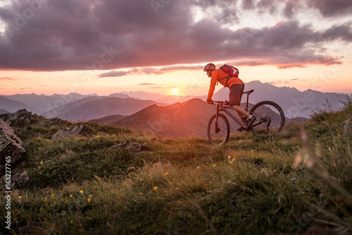 Fototapeta Męski mountainbiker przy zmierzchem w górach