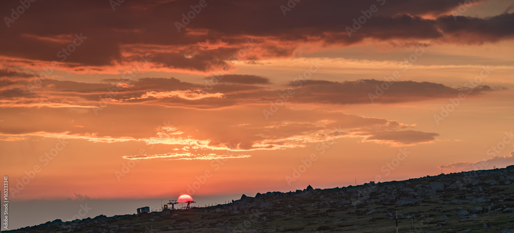 Fototapeta premium First rays of the summer sun, under dark stormy clouds - beautiful sunrise on a mountain top - July morning at Black Peak, Vitosha, Sofia, Bulgaria