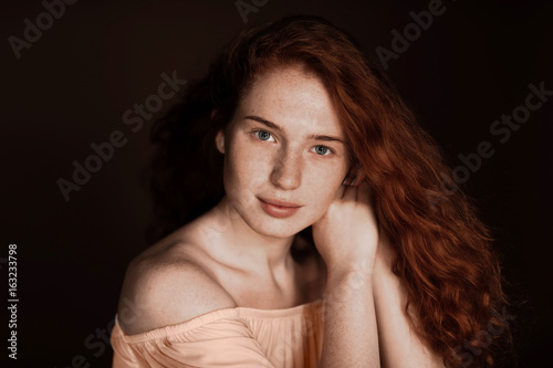 beautiful tender redhead woman with perfect skin posing in beige blouse, isolated on brown