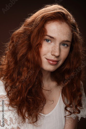 pretty redhead woman in white blouse smiling at camera, isolated on brown
