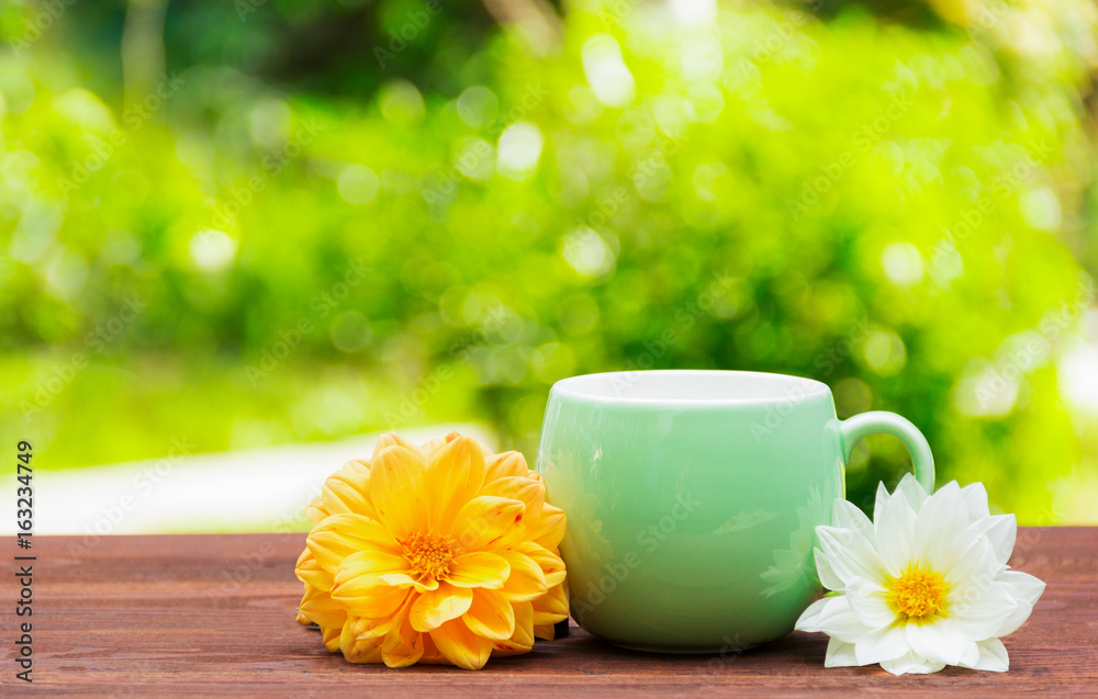 Mug with flowers on a green blurred background. A cup of tea in the summer garden. Copy space