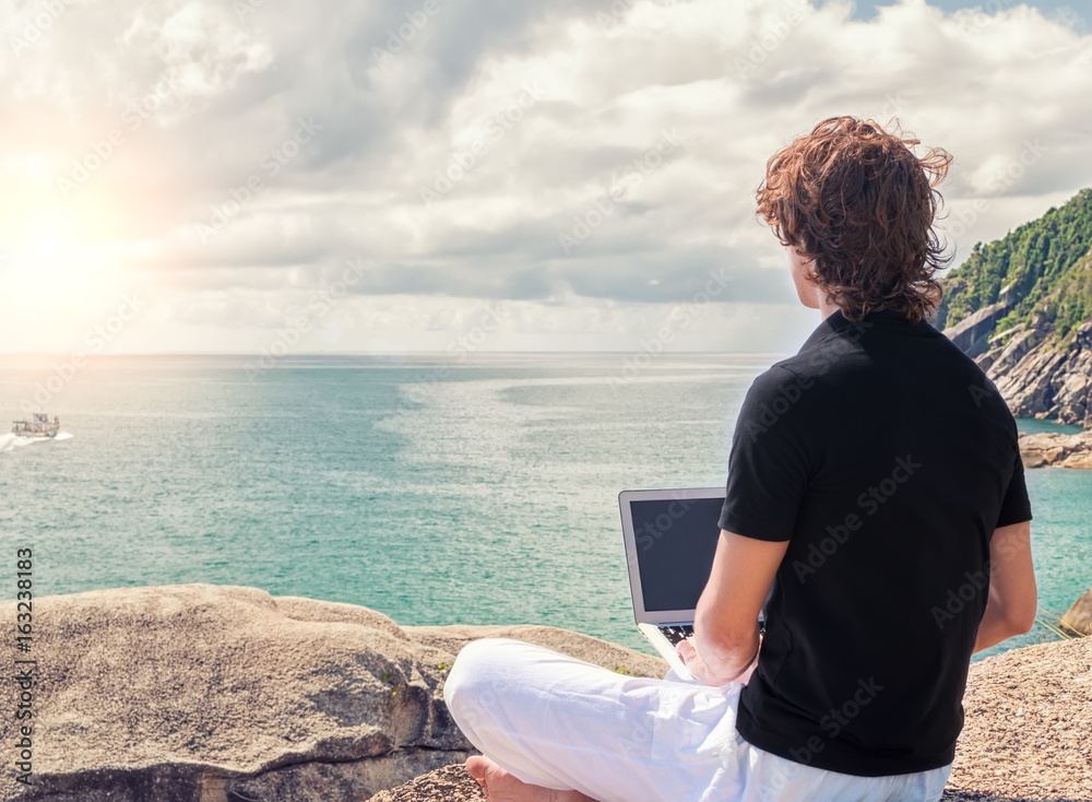 Man freelancer is sitting on the top of mountain and working with laptop during sunrise