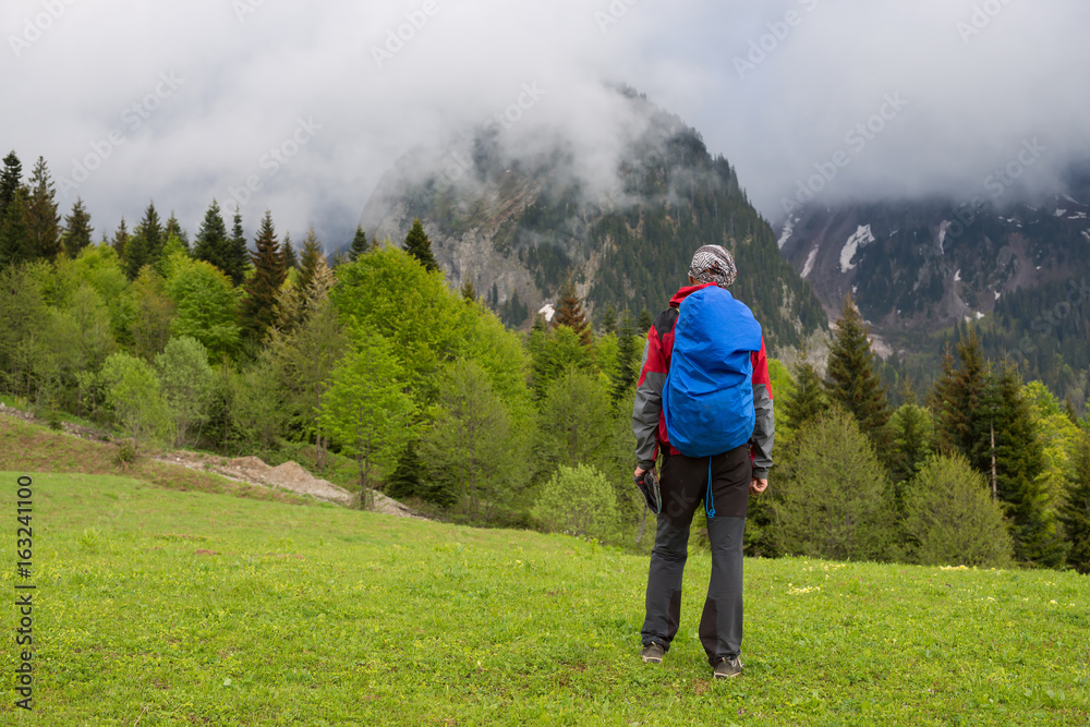 Man traveler is walks along alpine meadow after storm