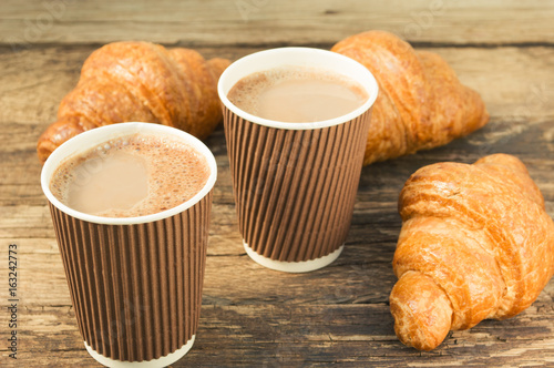 Tasty fresh croissants with coffee in a paper cup on old wooden background.