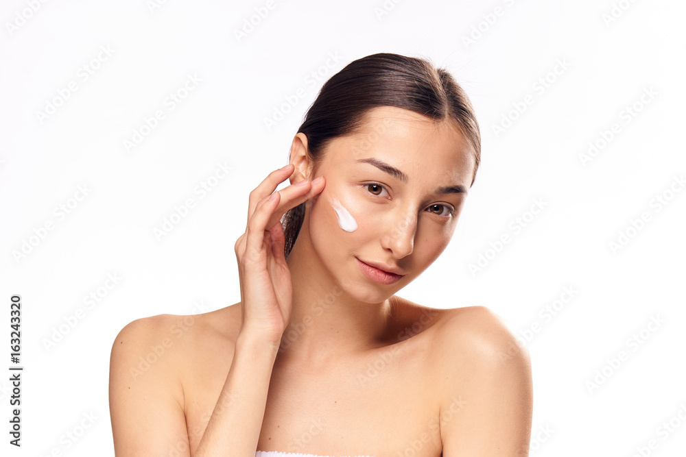 Beautiful young woman on white isolated background applies cosmetic face cream