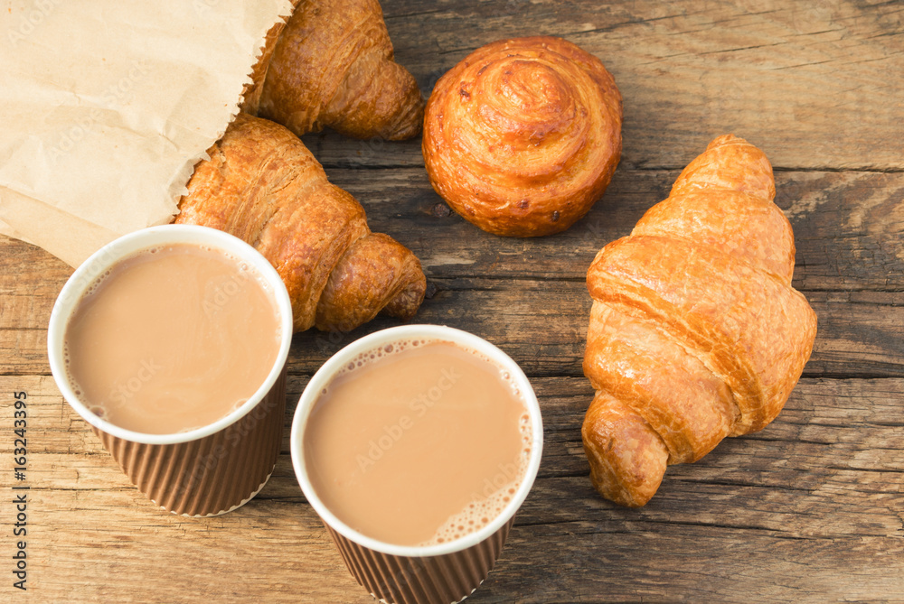 Tasty fresh croissants in paper beg and coffee in a paper cup on old wooden background. Tasty fresh croissants in paper beg and coffee in a paper cup on old wooden background.