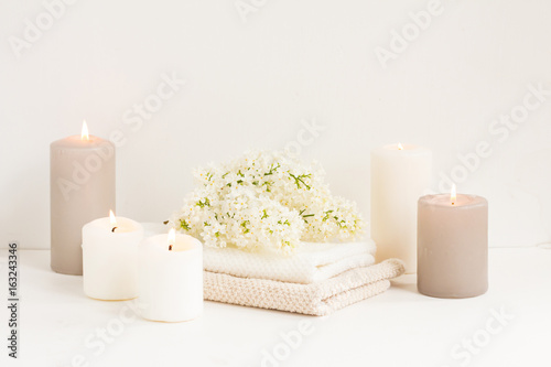 Spa composition. White candles, towel, lilac flowers on white wooden background.