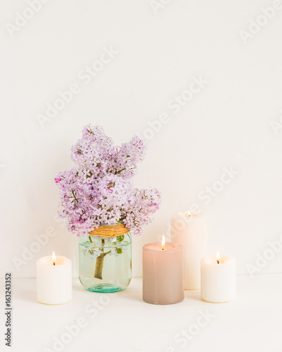 Spa composition. White candles  towel  lilac flowers on white wooden background.
