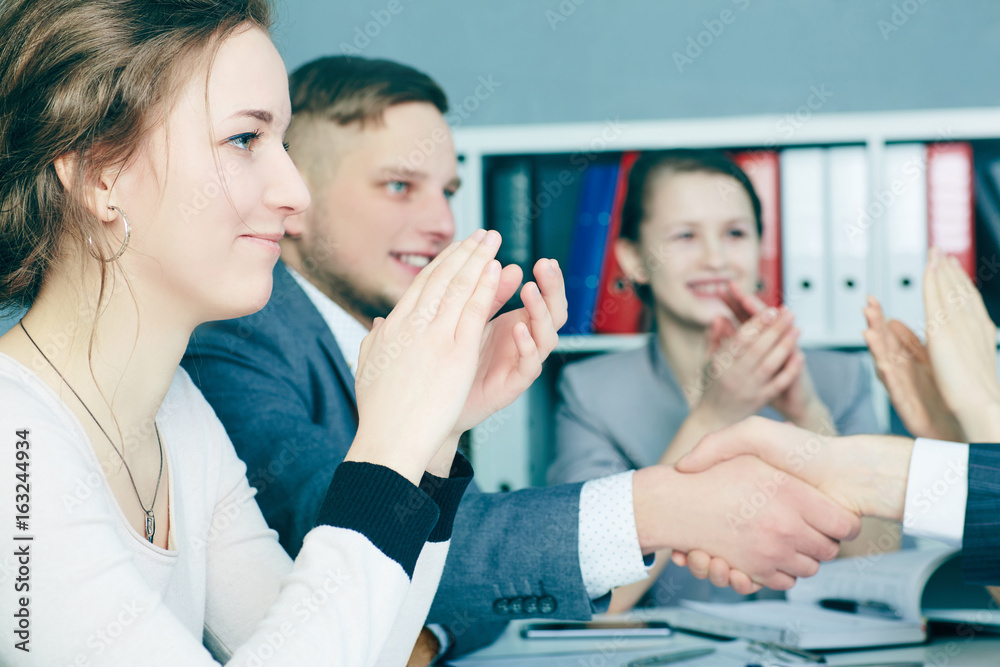 Business handshake. Close-up of two young man shaking hands with smile while sitting at office with their beautiful coworker. Business handshake. Close-up of two young man shaking hands with smile while sitting at office with their beautiful coworker.