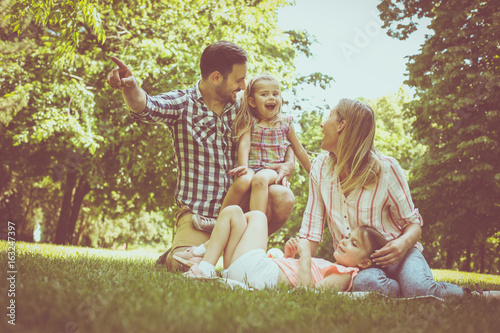Happy family sitting on grass in the meadow together and enjoying in summer day.
