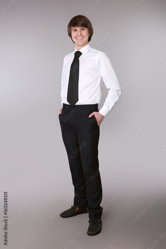 Cheerful employee man in white shirt with black tie keeping hands in pockets and smiling while standing isolated grey studio background. Cheerful employee man in white shirt with black tie keeping hands in pockets and smiling while standing isolated grey studio background.
