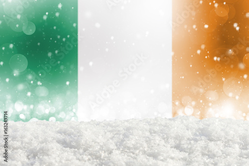 Defocused Ireland flag as a winter Christmas background with falling snow, snowdrift and bokeh
