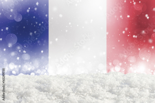Defocused France flag as a winter Christmas background with falling snow, snowdrift and bokeh