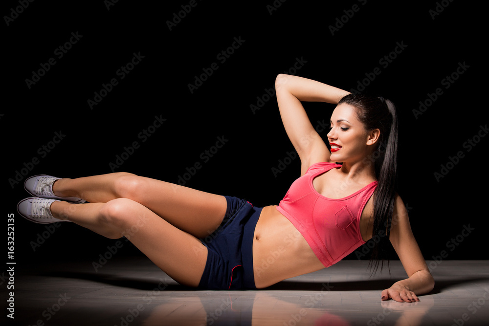 Obraz premium Portrait of happy sporty woman making abs exercise. Joyful female model training indoors. Healthy active lifestyle concept.