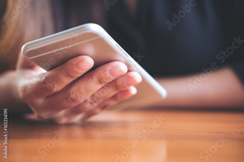 Closeup image of a woman holding and using smart phone on wooden table in office