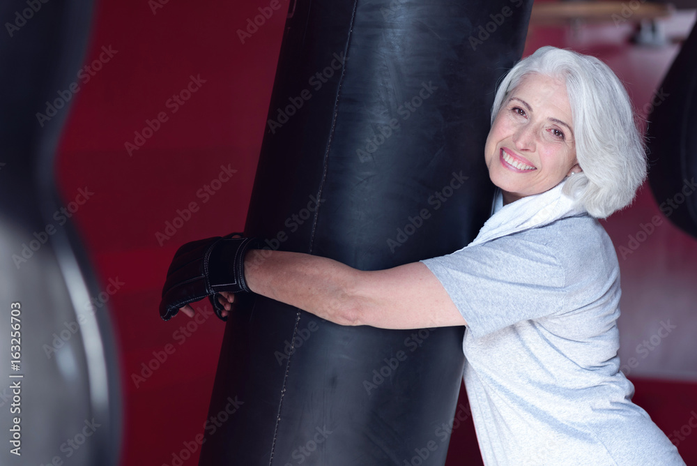 Vivacious aged woman hugging punchbag