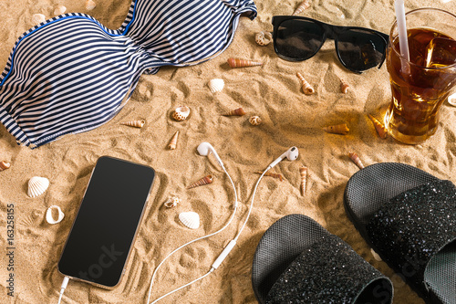 Summer bikini and accessories stylish beach set, Beach bikini summer outfit and sea sand as background, Top View, Concept photo