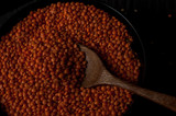 Heap of red lentils in a wooden bowl on dark background