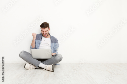 Young man playing on laptop sitting on floor