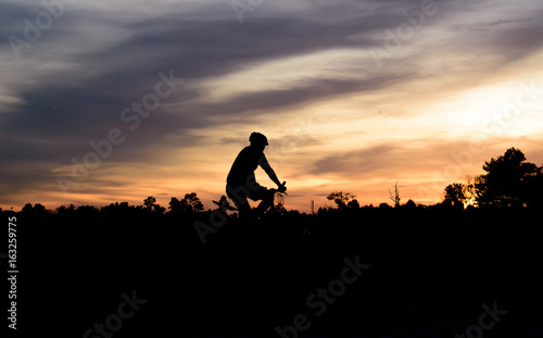 Silhouette of cyclist riding bike on road at sunset.