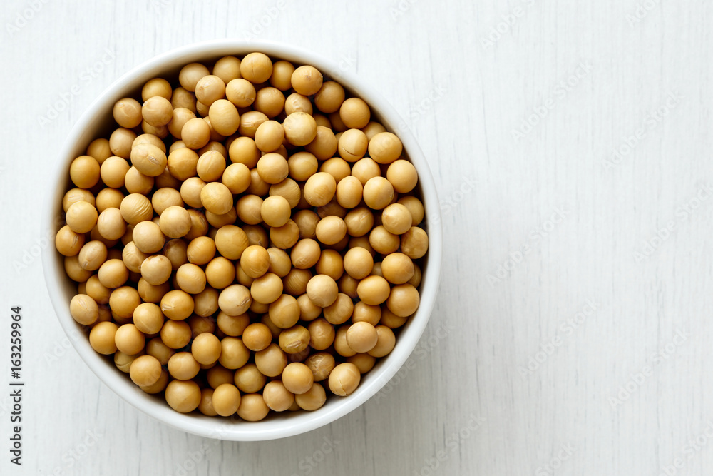 Dry soya beans in white ceramic bowl isolated on painted white wood. Dry soya beans in white ceramic bowl isolated on painted white wood.
