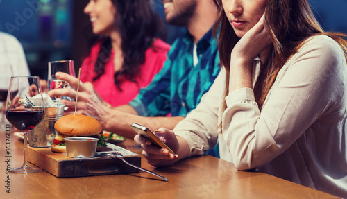 woman with smartphone and friends at restaurant