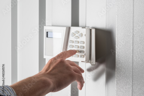 person typing on keypad of home security alarm, security system concept