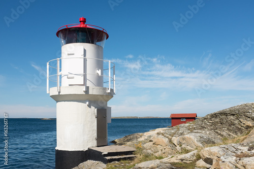 The beautiful little white lighthouse with its red ceilings  lit to control ships and boats  into the narrow passage into the beautiful Swedish archipelago   the horizon and the blue sky