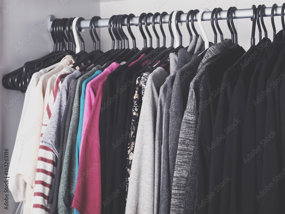 Obraz premium Woman's color-coordinated closet full of fashionable trendy clothes like t-shirts, blouses, sweaters, blazers, shirts and jackets. 