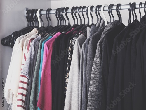 Woman's color-coordinated closet full of fashionable trendy clothes like t-shirts, blouses, sweaters, blazers, shirts and jackets.  © oprzybysz