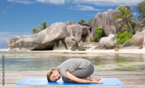happy woman doing yoga in child pose on beach