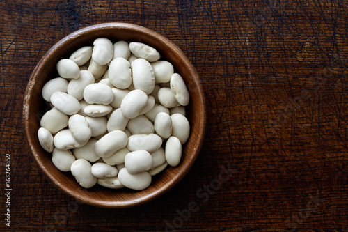 Dry butter beans in dark wooden bowl isolated on dark brown wood from above. photo