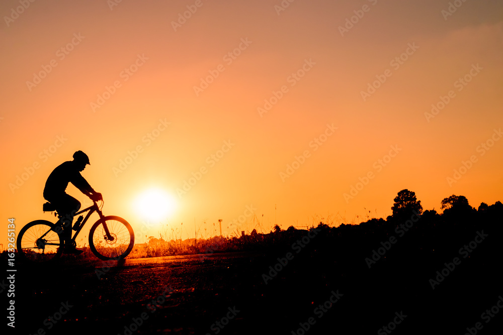 Fototapeta premium A man rides a bicycle in the evening with orange sky,Silhouette sporty image concept.