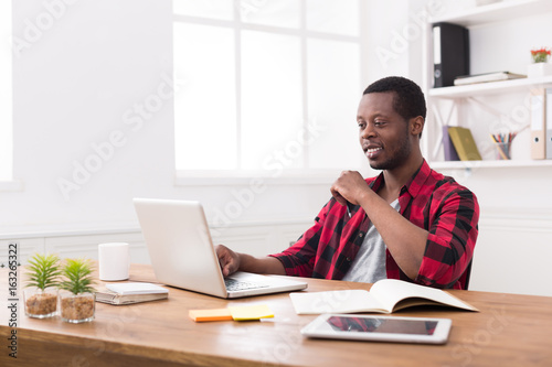 Smiling black businessman in casual office, work with laptop