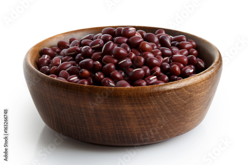 Dry adzuki beans in dark wooden bowl isolated on white.