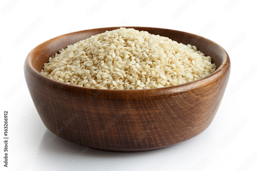 Decorticated sesame seeds in dark wooden bowl isolated on white. Decorticated sesame seeds in dark wooden bowl isolated on white.