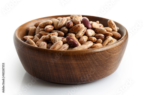Dry pinto beans in dark wooden bowl isolated on white.