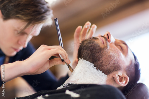 man and barber with straight razor shaving beard