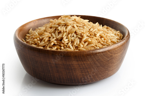 Uncooked long grain brown rice in dark wooden bowl isolated on white. 
