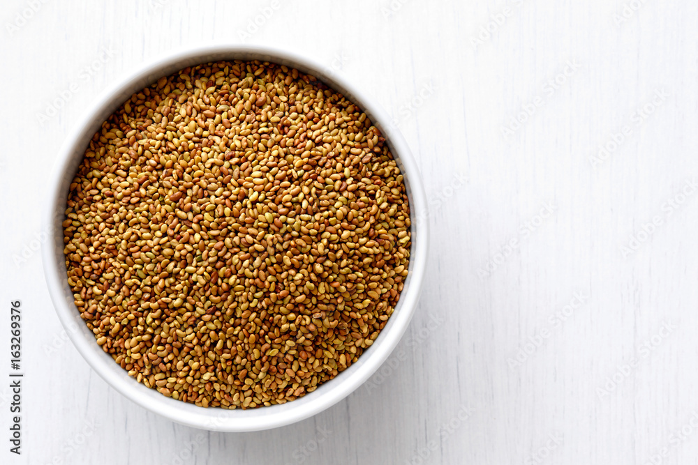 Alfalfa seeds in white ceramic bowl isolated on painted white wood from above. Alfalfa seeds in white ceramic bowl isolated on painted white wood from above.
