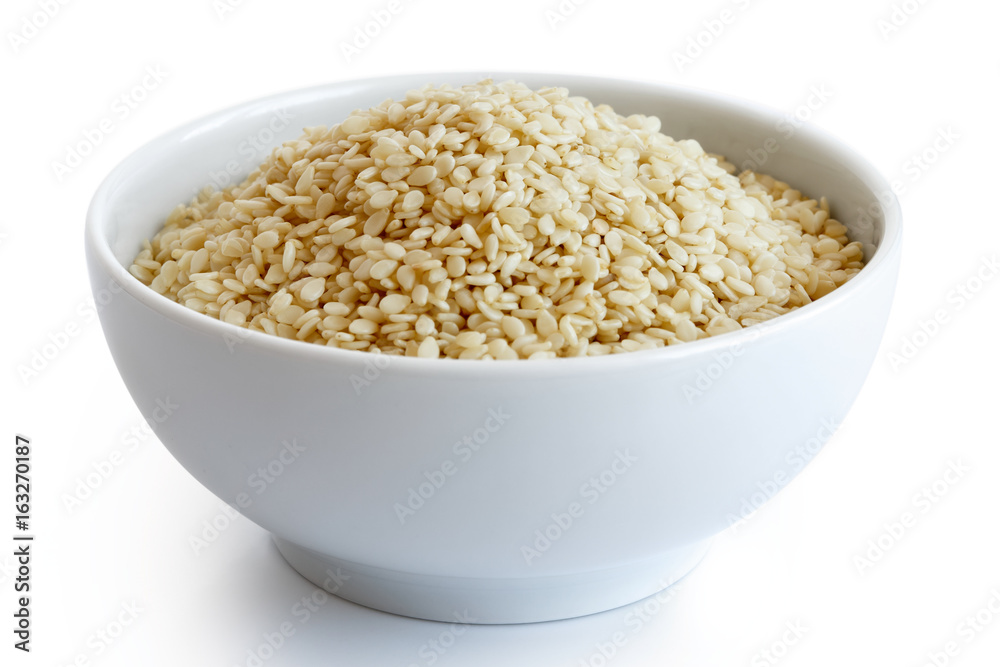 Decorticated sesame seeds in white ceramic bowl isolated on white. Decorticated sesame seeds in white ceramic bowl isolated on white.