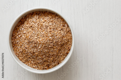 Wheat bran in white ceramic bowl isolated on painted white wood from above.  