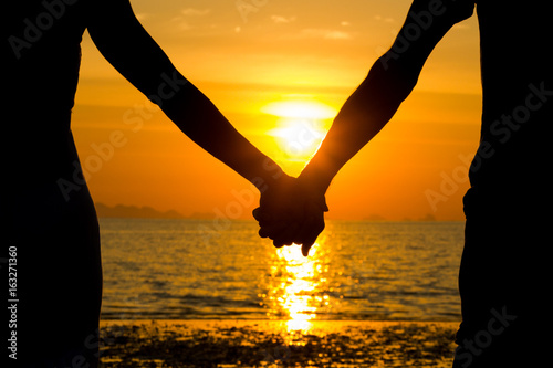 Perfect scene for Valentines Day with the silhouette of a couple holding hands at sunset by the sea in the island of Koh Phangan, Thailand. Romance, love concept