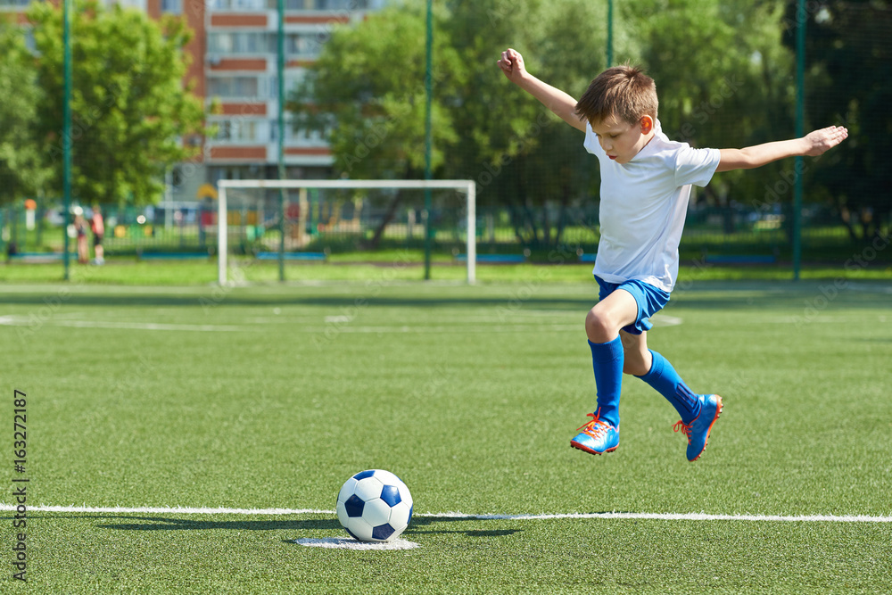 Boy soccer player with jump before kick on ball