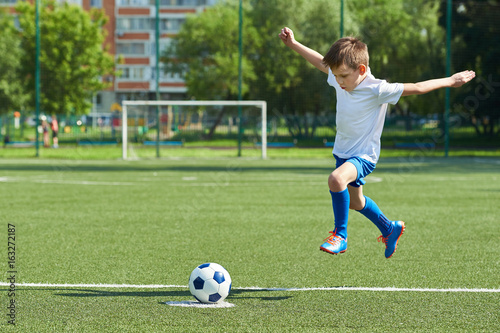 Boy soccer player with jump before kick on ball