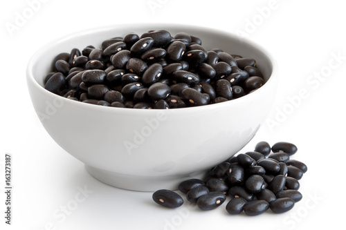 Black beans in white ceranic bowl isolated on white. Spilled seeds. photo