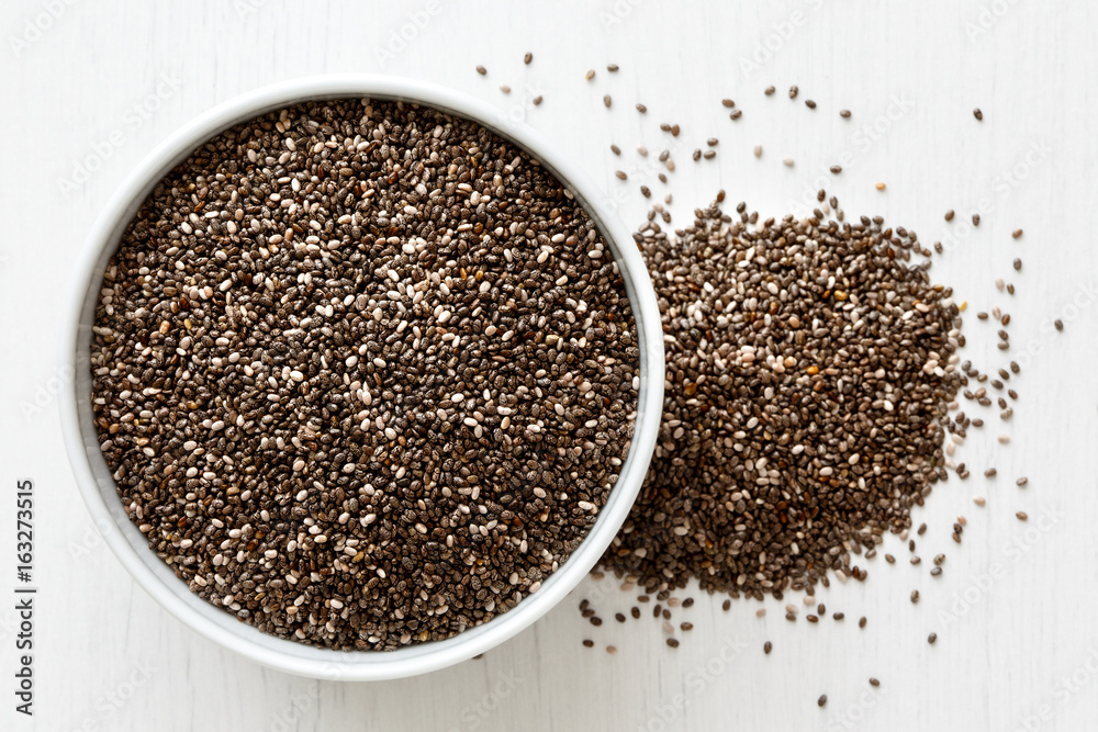 Chia seeds in white ceranic bowl isolated on painted white wood from above. Spilled seeds. Chia seeds in white ceranic bowl isolated on painted white wood from above. Spilled seeds.
