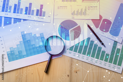 Magnifying glass and documents with analytics data lying on table,selective focus photo