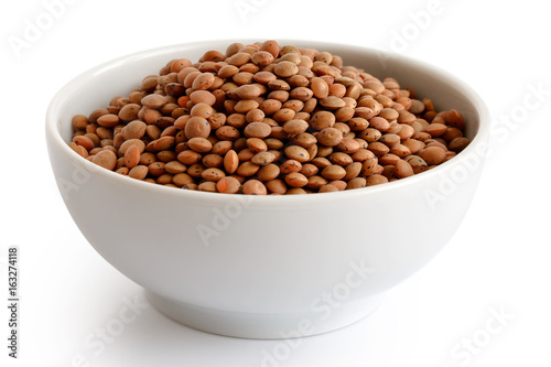 Dry unpeeled red lentils in white ceramic bowl isolated on white.
