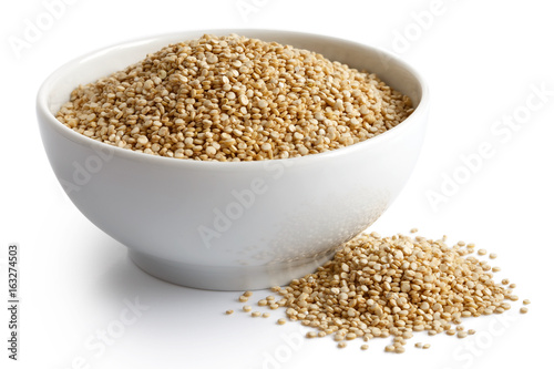 Quinoa seeds in white ceramic dish isolated on white. Spilled quinoa.